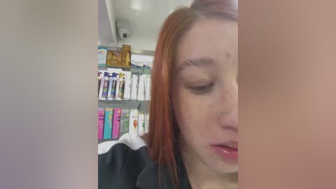 Video of a fair-skinned woman with long, red hair, eyes closed, smiling. She is in a brightly lit store with shelves of beauty products in the background.