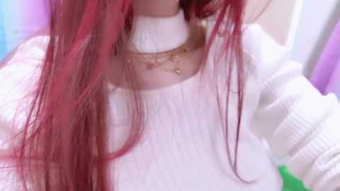 Video of a person with long, straight, vibrant red hair, wearing a white, chunky-knit sweater and a delicate gold necklace. Background is a blurred mix of pastel colors.