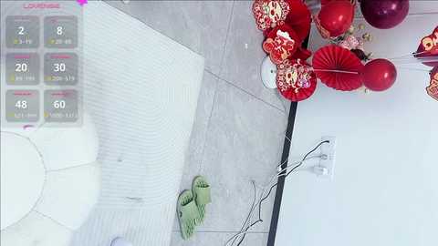 Video of a light grey tiled room with a white circular rug, green slippers, and a white chair. Red and white paper lanterns hang above a white wall, with a virtual reality interface overlay showing health and energy stats.