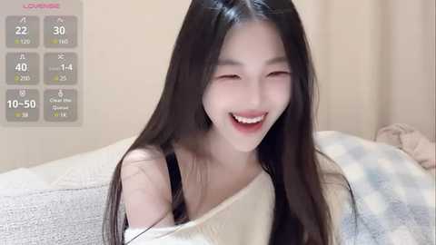 Media: A video of a young Asian woman with long black hair, fair skin, and a white off-shoulder sweater, smiling happily in bed. Background shows a digital thermometer display.