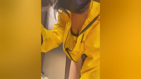 Media: Video of a woman in a yellow raincoat, partially bent over, with long black hair, touching a door handle in a dimly lit hallway.