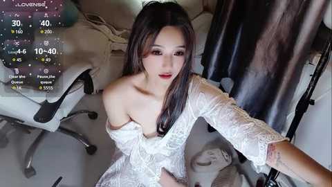 Media: Video of a young East Asian woman with long black hair, wearing a white lace dress, lying on a bed with a white chair, black curtains, and digital camera overlay.