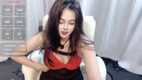 Media: A video of an Asian woman with long dark hair, wearing a red and black bra, sitting on a white chair, with a digital overlay showing viewer stats.