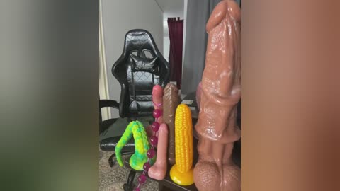 Video of a cluttered desk with various sex toys, including a large, realistic-looking penis and a cornucopia, next to a black gaming chair in a dimly lit room.