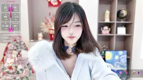 Media: Video of an Asian woman with straight, shoulder-length black hair, fair skin, and a slim build, wearing a white hoodie with a fluffy fur collar, indoors in a cozy room with a Christmas tree and shelves.