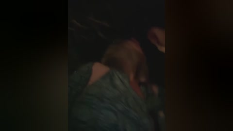 Media: A dimly lit video captures a person in a dark green jacket, lying on their side with their face partially obscured. The background is dark and indistinct.