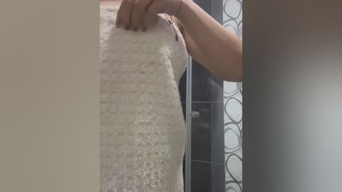 Video of a person's hand smoothing a white, fluffy textured foam insulation strip against a wall in a modern bathroom with tiled walls and a frosted glass shower door.