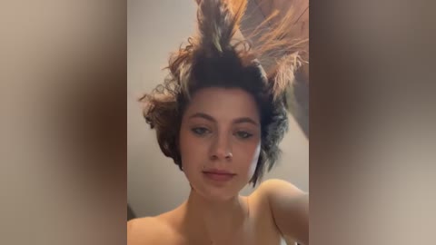 Media: A video of a woman with short, curly brown hair, styled into a voluminous, spiky hairstyle, wearing minimal makeup. Her expression is neutral. The background is blurred, focusing on her hair.