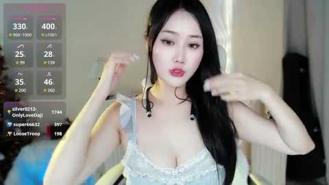 Media: A video of a young Asian woman with long black hair and fair skin, wearing a white lace bra, posing in a dimly lit room.