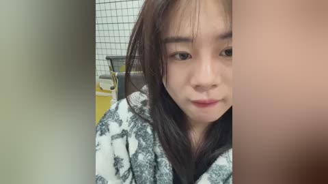 Media: Video of a young Asian woman with straight, dark hair, wearing a white bathrobe with black patterns, sitting in a tiled bathroom.