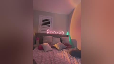 Video of a cozy, pastel-themed bedroom with a pink fluffy blanket, a light-colored bed, and a \"Jordan XOXO\" sign, lit by warm, soft lighting.