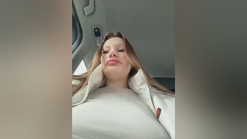 Video of a young woman with long, straight light brown hair, wearing a beige sweater, reclining in a car seat, with her head resting on the window frame.