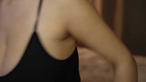 A close-up video of a woman's bare shoulder and arm, wearing a black tank top. The background is blurred, suggesting an indoor setting.