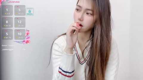 Media: A video of a young Asian woman with long, straight brown hair, wearing a white school uniform, biting her finger against a plain white background.