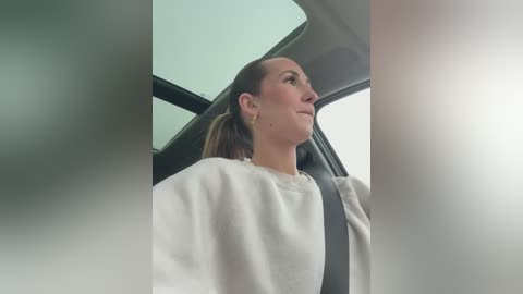 Media: A video of a Caucasian woman with brown hair tied back, wearing a white sweatshirt, seated in a car, looking out the window.