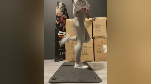 Media: A video of a woman in gray leggings and white sneakers balancing on a balance board in a cluttered room with cardboard boxes and a shopping bag.