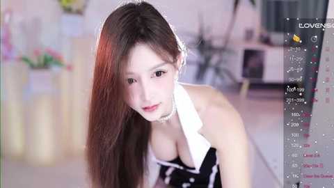 Media: Video of an Asian woman with long, straight brown hair, wearing a black and white maid outfit, leaning forward with a serious expression. Background shows a blurred indoor setting with flowers.