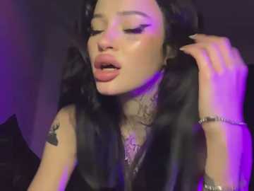 Media: Video of a woman with long black hair, fair skin, and closed eyes, wearing a black top, with a tattoo on her left arm, and purple lighting, creating a sensual, intimate atmosphere.