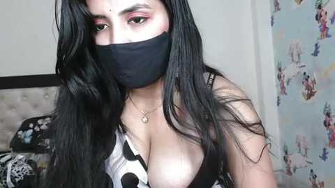 Media: A video of a woman with long black hair, wearing a black mask and a black-and-white patterned top, partially exposing her cleavage. Background shows a bed and colorful anime posters.