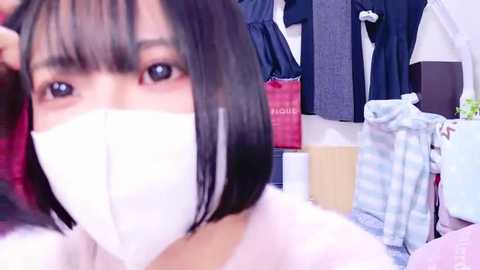 Media: A video of a young woman with short black hair, wearing a white face mask, standing in a room with a pink jacket, blue striped shirt, and a red shopping bag.