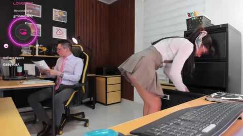 A video of a modern office with two white men, one seated at a desk, the other bending over a keyboard. The office features vibrant wall decor and a pink neon sign.