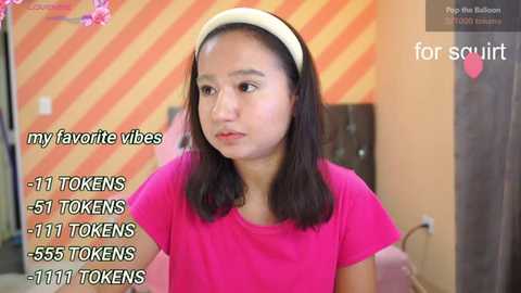 Video of a young woman with medium skin tone and straight black hair, wearing a pink t-shirt. Background features orange and yellow striped wallpaper. Text overlay reads \"my favorite vibs: 11 TONS, 51 TONS, 55 TONS - 1111 TONS.\