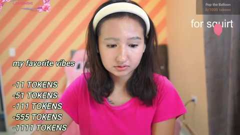 Video of a young Asian girl with straight black hair, wearing a pink shirt and white headband, against a striped background. Text overlays show 11 tokens, 51 tokens, 55 tokens, and 1111 tokens.