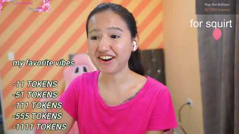 Media: Video of a young woman with light brown skin, dark hair, wearing a pink t-shirt, smiling, in a room with orange-striped walls and a pink chair, with text overlay mentioning TikTok views.