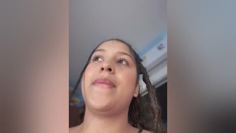 Media: A close-up video of a young girl with dark skin and curly hair, smiling and looking up. The background is blurred, showing a ceiling with a light fixture.