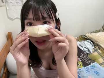 Media: Video of an Asian woman with long black hair, wearing a white sleeveless top, covering her face with a large piece of white tape. Background includes a wooden bed with a plaid blanket and a white wall.