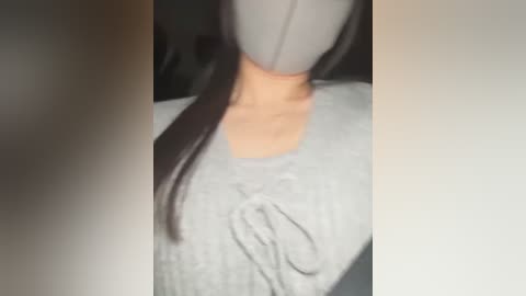 Media: A blurred video of a woman with long, straight black hair, wearing a gray top with a subtle bow design, against a dark background.