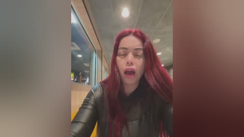 Video of a young woman with long, red hair, wearing a black leather jacket, screaming in a modern office setting.