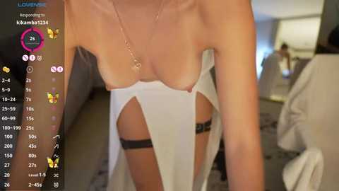 Media: Video of a woman with light skin, wearing a white, sheer, strapless top that reveals her breasts and black lingerie. Background shows a blurred room with modern decor.