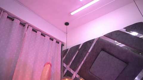 Media: Video of a modern, minimalist room with gray curtains, a dark couch, and a pinkish-purple ceiling light. A large, erect penis is prominently featured in the foreground, partially obscured by the curtains.