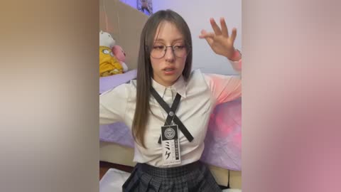 Media: Video of a young Asian woman with long straight brown hair, glasses, and a white shirt with a black tie, sitting on a bed with plush toys, making a hand gesture.