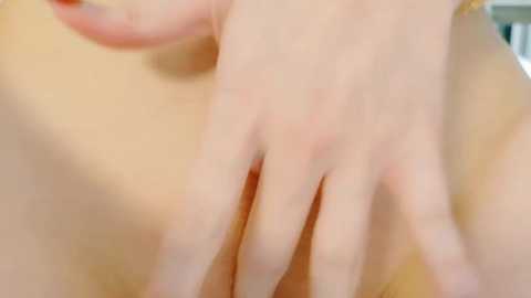 Media: A close-up video of a fair-skinned, nude woman's hand resting on her stomach, fingers lightly touching her skin. The background is blurred, suggesting an indoor setting.