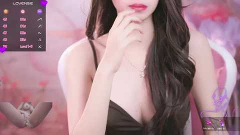 Video of a fair-skinned woman with long, dark hair, wearing a black lace top, and red lipstick, against a soft pink and purple background.