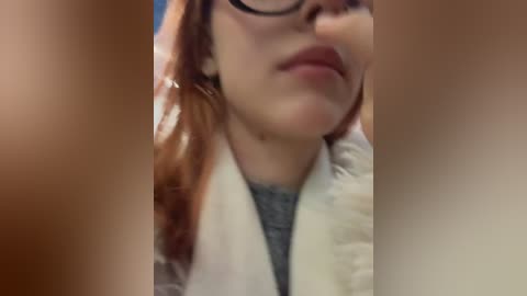 Video of a close-up, blurred face with fair skin, red hair, black-rimmed glasses, and a grey shirt, set against a blurred background.