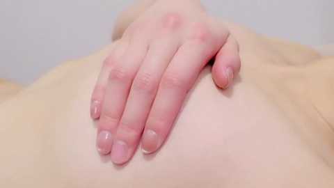 Video of a pale-skinned hand with short nails gently touching a smooth, light-colored skin surface, likely a person's back or abdomen, set against a plain, light background.