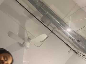 Media: Video of a ceiling with a white fan and a silver HVAC duct running horizontally. The ceiling is white, and there are visible wires and a light bulb in the lower left corner.