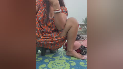 Media: A video of a woman in an orange floral dress squatting on a blue and green patterned rug, partially obstructed by a red filter.