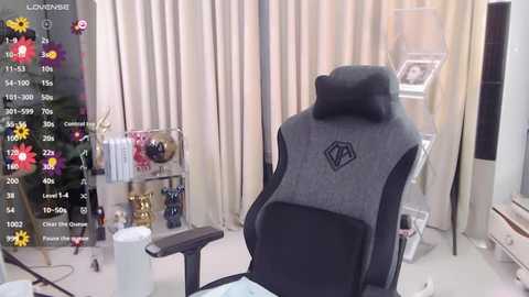 Video of a modern gaming room with a grey and black gaming chair, beige curtains, a white desk, and colorful flowers on the left.