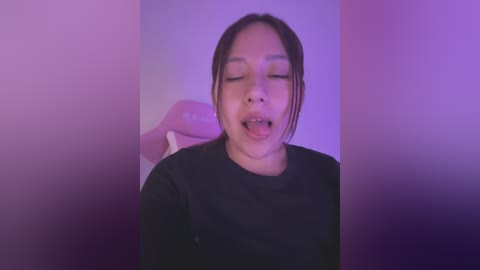 Media: Video of a smiling Asian woman with medium skin tone, wearing a black shirt, eyes closed, mouth open, in a purple-lit room, blurry background.