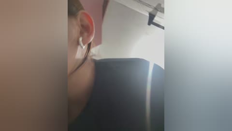 Media: Video of a close-up view of a person's ear with a white earbud, showing the inner ear canal. Background features a blurry, light-colored ceiling and a dark object, possibly a door or cabinet.