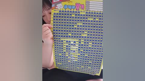 Media: Video of an Asian woman with short black hair peering through a large, colorful, square puzzle with blue and yellow pieces, partially obscuring her face.