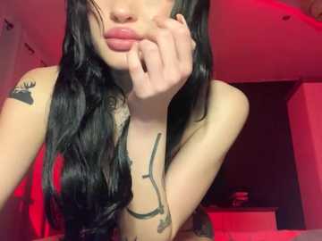 Media: Video of a young woman with long black hair, light skin, and a red bra, standing in a dimly lit room with red lighting. She has tattoos on her arms, and her right hand is near her mouth.