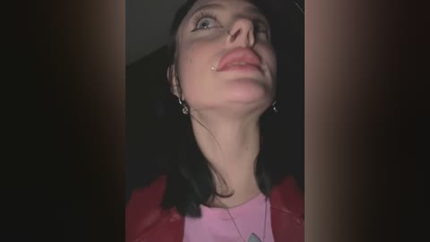 Video of a young woman with fair skin, long black hair, and a red jacket, wearing a surgical mask with a clear tube attached to her nose, looking up in a dimly lit room.