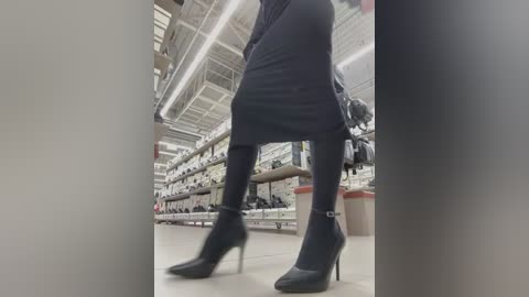 Video of a person in a black dress and black high-heeled boots walking in a spacious, modern clothing store with high ceilings and shelves filled with clothing.