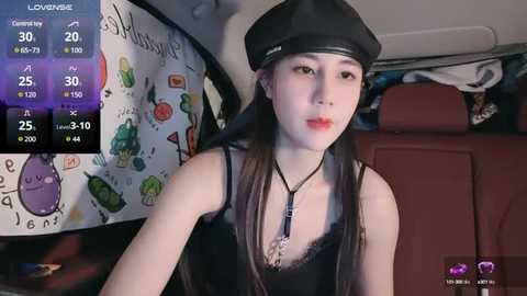 Media: Video of a young Asian woman with long black hair, wearing a black beret and a black lace camisole, seated in a car with a colorful, artsy interior.