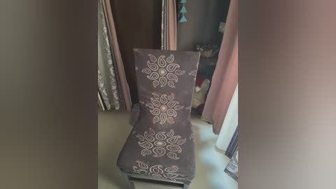 Media: Video of a brown cushioned chair with intricate white mandala patterns, surrounded by pink and white curtains in a dimly lit room.